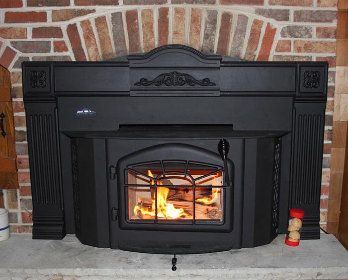 Mason's Chimney Service Original Photo of Wood Stove Insert black wood burning stove insert set in a brick surround with a stone hearth